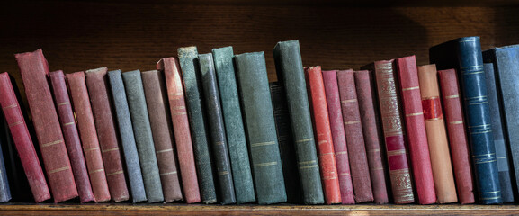 Collection of colorful old books on a shelf, library or knowledge background, panoramic view of ancient wooden bookcase