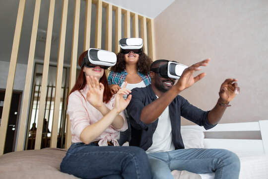 Family, african father, caucasian mother and cute excited teen daughter, waving hands and touching air while trying VR glasses at home