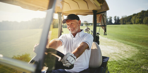 Smiling senior man driving his golf cart on a fairway