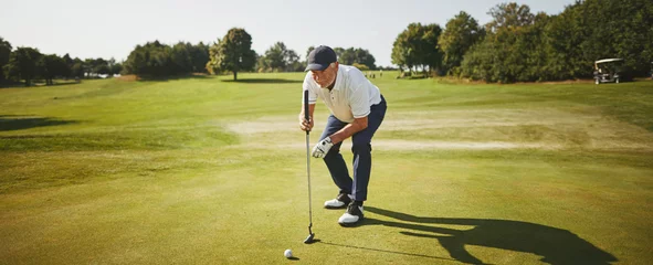 Poster Senior man preparing to putt on a golf green © Flamingo Images