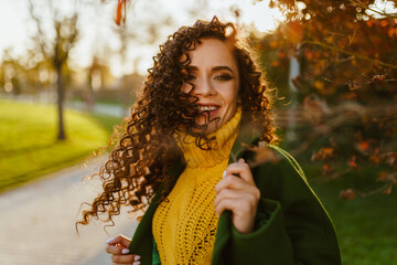 a girl with curly brown hair and a charming smile circling her head so that her hair fluttered in the wind and smiles holding on to the lapel of her coat in the park in the autumn. High quality photo