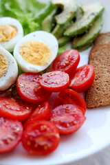 Boiled eggs, bacon, avocado, toast and tomatoes and lettuce salad.