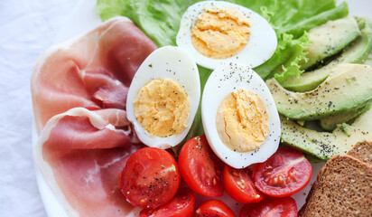 Boiled eggs, bacon, avocado, toast and tomatoes and lettuce salad.