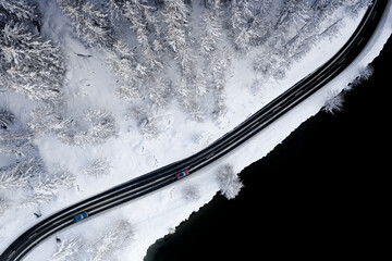 Cars driving on icy road through snowy woods at the edge of Lake Sils, aerial view, Engadine, Graubunden Canton, Switzerland, Europe
