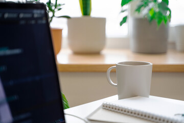 The laptop on a white desk in a bright office, the code on the screen