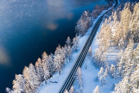 Empty road crossing the winter forest covered with snow beside Lake Sils, aerial view, Engadine, Graubunden Canton, Switzerland, Europe - Powered by Adobe