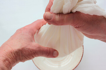 Old woman hands holding a homemade cottage cheese in cloth on white background. Ricotta cheese making process. Top view.
