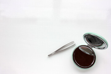 Eyebrow tweezer and compact makeup mirror on a white background. Beauty and care concept. Top view, copy space. 
