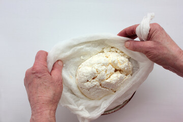 Old woman hands holding a homemade cottage cheese in cloth on white background. Ricotta cheese making process. Top view.
