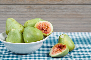 Green figs in a white bowl and on a wooden table with blue tablecloth