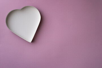 An empty, white heart-shaped box on a pink background with a pattern of small, darker pink dots. 