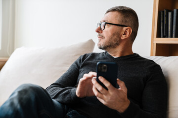 Serious adult unshaven man using cellphone while resting