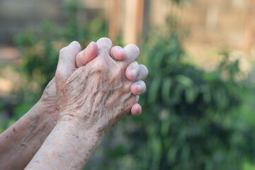 Close-up of senior woman's hands joined together for praying while standing in a garden. Focus on hands wrinkled skin. Space for text. Concept of aged people and healthcare