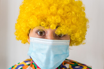 Linda mujer joven sonriendo mientras está vestida con un disfraz de payaso con una mascarilla quirúrgica desechable y una peluca de payaso amarilla. Protección contra el virus sars-cov-2