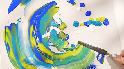Drawing multicolored picture using metal palette knife. Large strokes of multi-colored paint. Mixing acrylic paint. Oil paint smeared across the canvas. Drops of paint on canvas close up