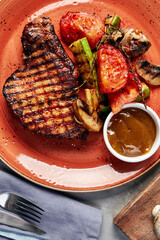 chop cooked on the grill with vegetables on a plate with sauce on a gray concrete background top view