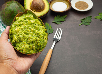 Fresh guacamole with ingredients for homemade guacamole: avocados, lemon, salt, and pepper. Space for text. Close-up photo. Concept of healthy fruits and traditional Mexican preparation
