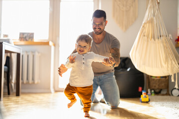 Happy father helping little son walking in living room
