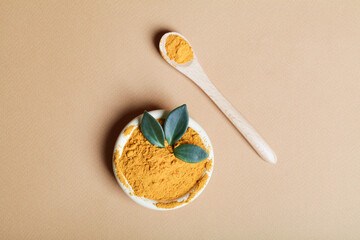 diet nutrition, health care lifestyle concept. Curcuma Longa or turmeric powder in bowl with green leaf and wooden spoon on beige background