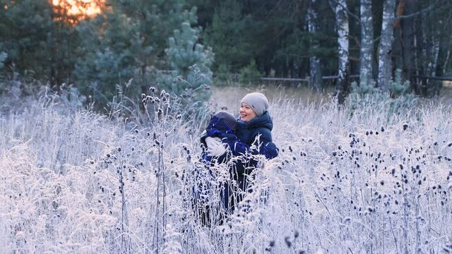 The boy and mum run towards each other with outstretched arms. Family in the winter outdoors. People walk through the snow-covered forest in the evening at sunset. Beautiful fabulous natural landscape