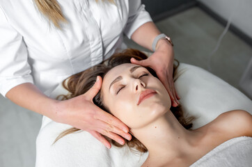 Fototapeta na wymiar Facial massage of young woman receiving spa massage in beauty spa. Cosmetology.