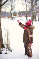 A little boy lays down bread in a bird feeder on a winter day.