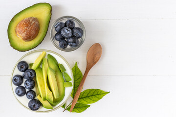 Top view of organic yogurt topped with avocado and blueberry on white wooden background, healthy and nutritious diet