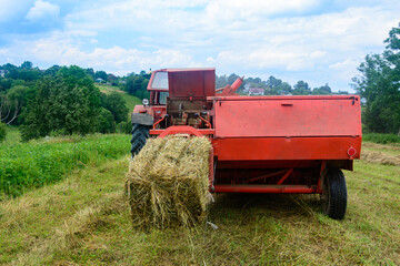 Obraz premium Pressing hay into bales, old working press, harvesting and harvesting dry fodder.