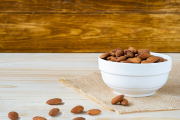 Almonds in white porcelain bowl on wooden table with wooden background and copy space for text.