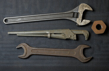 An old open-end and adjustable wrench and a gas wrench on a dark background and a rusty nut. Renovation concept.