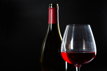 Wine bottle and glass with red wine on dark glossy background.