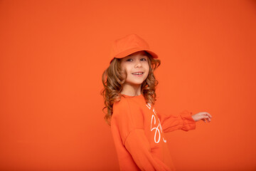 Beautiful child girl 6-7 years old in orange cap with place for text, mock up. Studio shot, Printing on textiles, production of hats. Showing hand