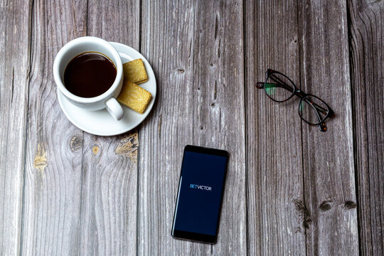 02-24-2021 Portsmouth, Hampshire, UK A mobile phone or cell phone on a wooden table with the Bet Victor app open next to a coffee and glasses