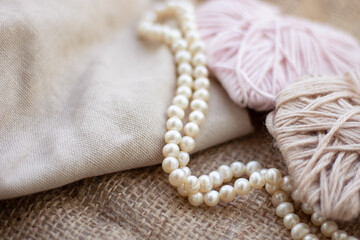 Cuts of yarn and thread on the background of burlap. Beige and soft pink colors of woolen and acrylic threads. There are pearl beads on the balls. Still life. Sackcloth. Fabric background