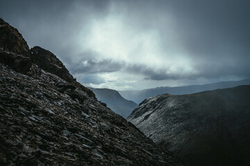 Dark atmospheric landscape on edge of abyss in highlands. Dangerous mountains and abyss in overcast weather. Danger mountain pass and sharp rocks under gray sky. Dangerous rainy weather in mountains.