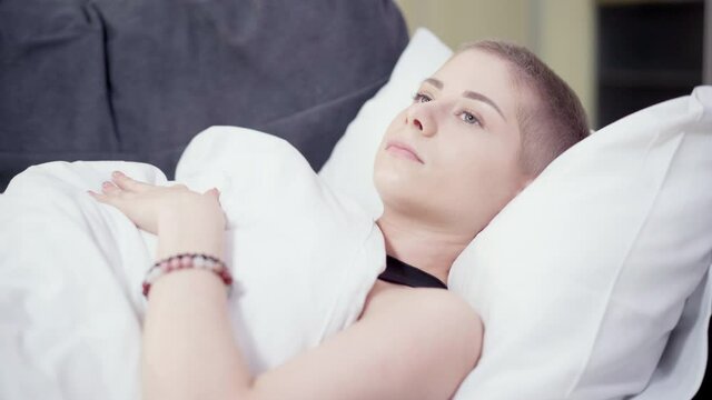 Portrait of desperate young woman having cancer lying on couch thinking. Tired young frustrated Caucasian patient resting after chemotherapy indoors. Fatigue and hopelessness.