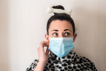 Mujer joven vestida con un disfraz de troglodita, mujer de las cavernas con un hueso en la cabeza. La chica lleva una mascarilla desechable azul que cubre su boca para protegerse del virus Sars-CoV-2