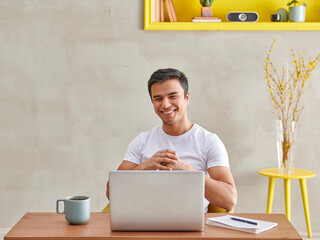 Happy Uzbek man is working and video talking head of laptop, coffee yellow niche style.