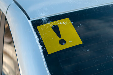 The Novice driver sign on the rear window of the car. A yellow square sticker with a black exclamation mark on the body of cars driven by drivers with less than two years of experience.