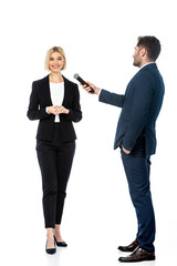 full length view of anchorman with hand in pocket taking interview from smiling businesswoman on white