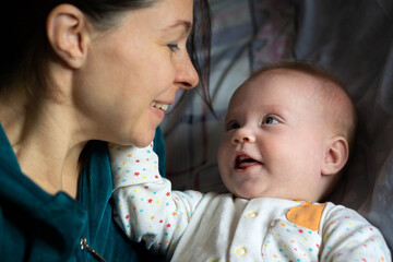 Crop woman toothy smiling while looking at adorable baby in bedroom at home.