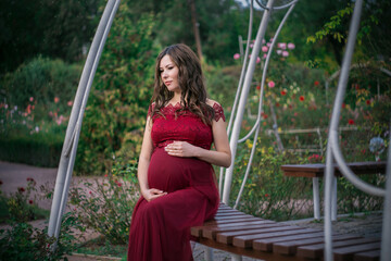 Pregnant woman resting in spring blooming garden. Posing outdoors. Motherhood. High quality photo.