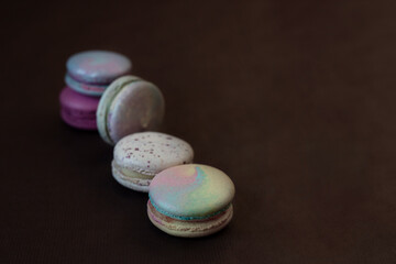 Small cake macarons made from chopped almonds and meringues of different colors lie on a brown background