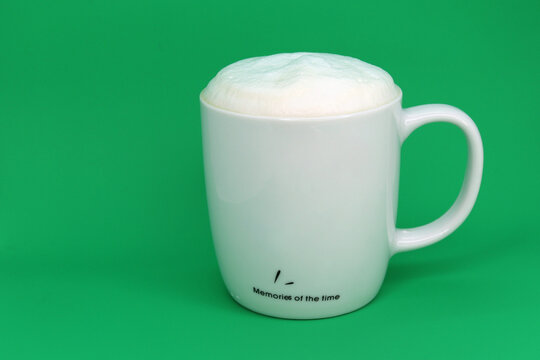 Coffee with foam in a white mug on a green background