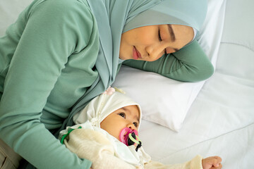 Asian Muslim new born baby wearing HIJAB with mother sleeping on white bed