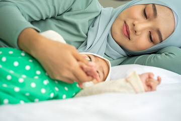 Asian Muslim new born baby wearing HIJAB with mother sleeping on white bed