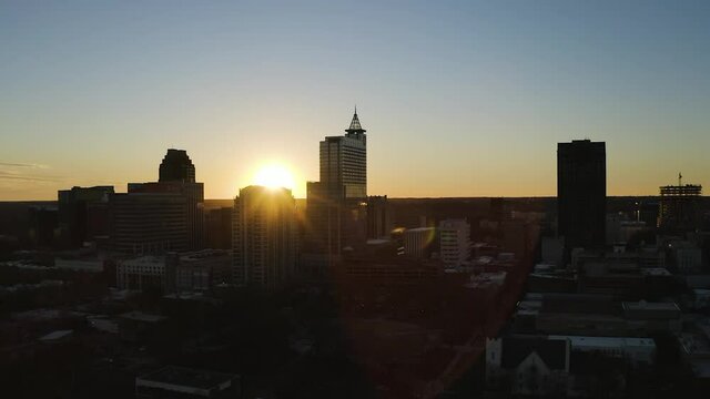 Sunset at the horizon behind the skyscrapers of the skyline of Downtown Raleigh on a bright sunny summer day. Drone panning shot