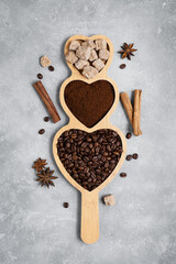 Coffee beans, ground coffee, brown sugar cane, star anise and cinnamon on a wooden stand on a gray...