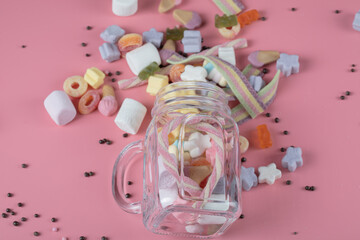 Mix of marshmallow and jellybeans on a pink background out of cups