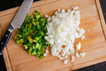 Chopped Green Bell Pepper and Onion on a Bamboo Cutting Board: Overhead view of diced vegetables on...